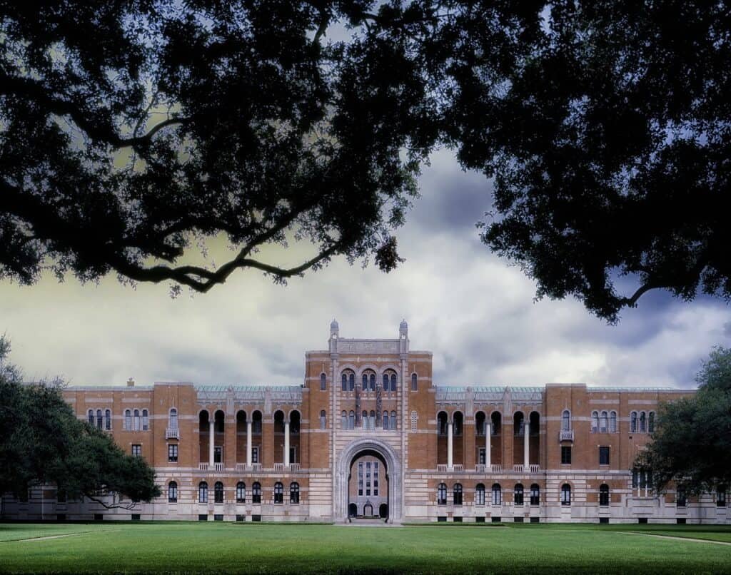 Image of Rice University under a cloudy sky, framed by pine branches from a nearby tree. Featured image for the page about applying to graduate school.